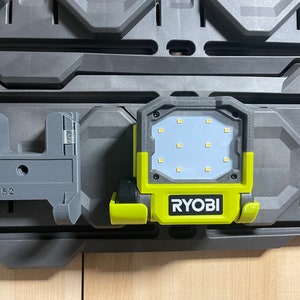 以下が含まれることがあります： グレーとイエローのRyobiワークライト。白いLEDパネルと12個のライトが付いています。ライトは、「FVL52」と印刷されたグレーの壁オーガナイザーに取り付けられています。