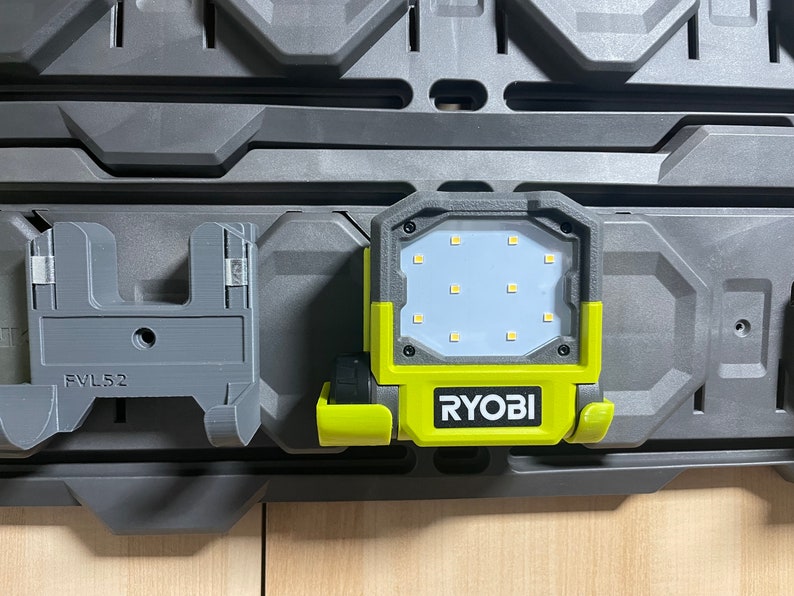 以下が含まれることがあります： グレーとイエローのRyobiワークライト。白いLEDパネルと12個のライトが付いています。ライトは、「FVL52」と印刷されたグレーの壁オーガナイザーに取り付けられています。