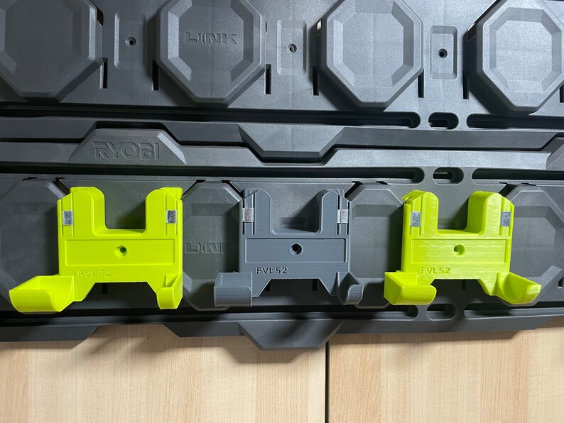 以下が含まれることがあります： Ryobi ツールシステム用のツールホルダー3個。ホルダーはプラスチック製で、緑とグレーです。ホルダーには「FVL52」と「RYOBI」のラベルが付いています。