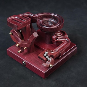 May include: A wooden marble run with a complex track design. The run is made of dark red wood and features a spiral track, a switch, and a drop. The run is powered by a small motor and includes several steel marbles.