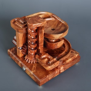 Könnte beinhalten: Eine Holz-Murmelbahn mit einer Spiralbahn, einer gebogenen Bahn und einer kleinen Holzschale oben. Die Murmelbahn ist aus dunkelbraunem Holz mit natürlicher Holzmaserung.