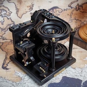 Può includere: Una pista per biglie cinetica in legno nero con un sistema a spirale a più livelli e sfere in ottone. La struttura comprende un meccanismo di sollevamento, pilastri di supporto verticali e una piccola targa in ottone sulla base.
