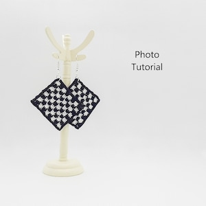 Puede incluir: Pendientes de crochet con patrón de tablero de ajedrez colgados de un expositor blanco. Los pendientes son negros y blancos y tienen forma cuadrada. Tutorial fotográfico.