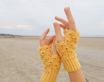 May include: A pair of yellow crocheted fingerless gloves with a lacy pattern. The gloves are held up in the air with the fingers extended.