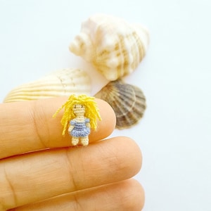 May include: A tiny crocheted doll with yellow yarn hair and a blue dress. The doll is being held between two fingers.