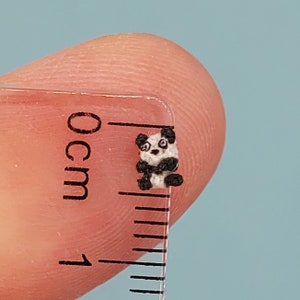 Puede incluir: Un pequeño oso panda de crochet, de aproximadamente 1 cm de tamaño, se muestra junto a una regla.