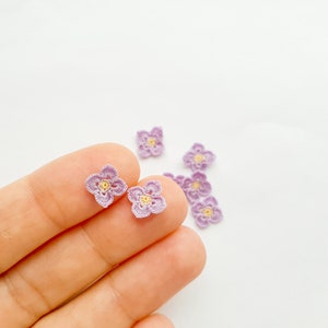 May include: A close-up of a hand holding several small crocheted flowers. The flowers are purple with yellow centres.