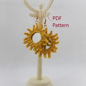May include: A pair of crocheted sun earrings in a bright yellow color. The earrings are displayed on a white stand. The text "PDF Pattern" is visible in the image.