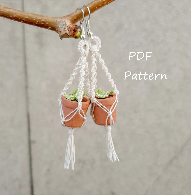 May include: A pair of white macrame plant hanger earrings with small terracotta pots and green plants. The earrings are hanging from a branch. The text "PDF Pattern" is written in white on a gray background.
