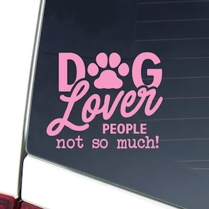 May include: Pink vinyl decal with the words "Dog Lover" and a paw print graphic. Below the text, it reads "People not so much!" The decal is designed to be applied to a car window or similar surface.
