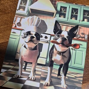 May include: Two Boston Terrier dogs dressed up in a kitchen setting. One dog is wearing a chef's hat and a pink and white striped apron. The other dog is holding a wooden spoon in its mouth.