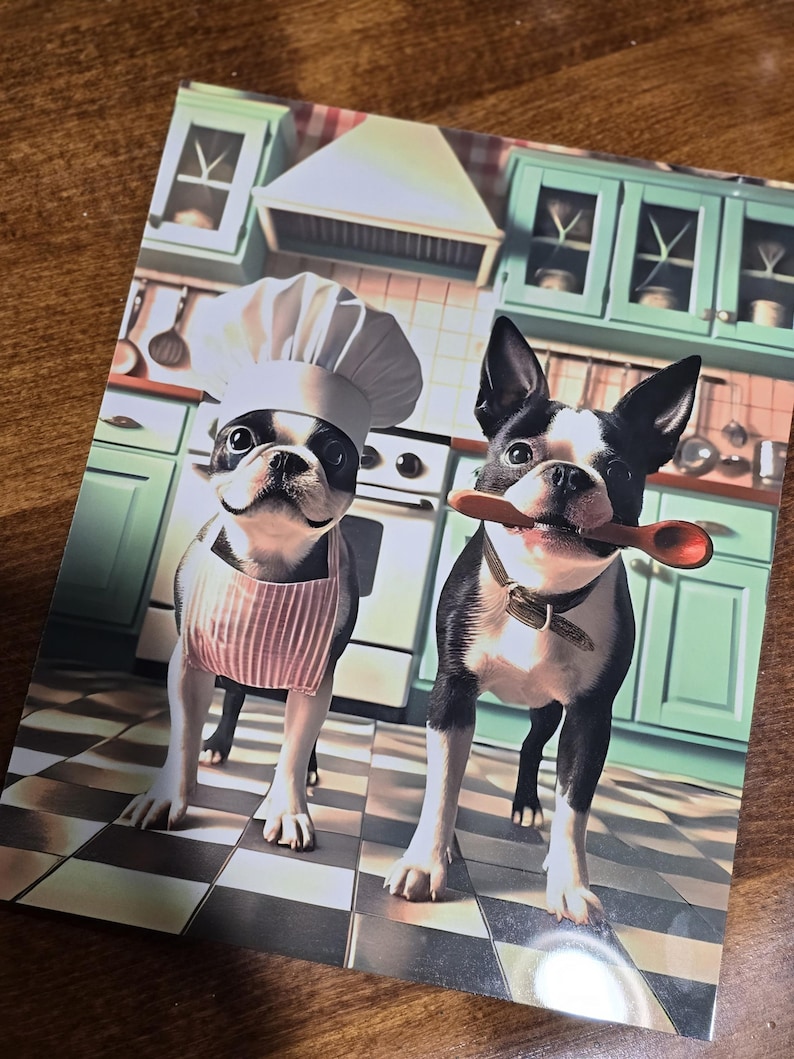 May include: Two Boston Terrier dogs dressed up in a kitchen setting. One dog is wearing a chef's hat and a pink and white striped apron. The other dog is holding a wooden spoon in its mouth.