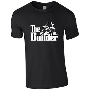 May include: A black short-sleeved t-shirt featuring a white graphic print. The design shows a hand operating a marionette crossbar, with a trowel, bricks, hammer, and tape measure hanging as puppets. The text reads The Builder in white lettering.