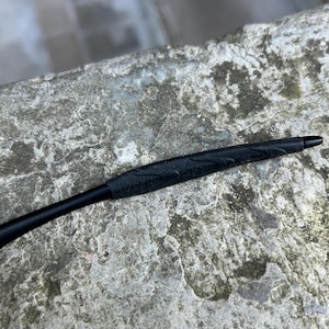 May include: A black pen with a textured grip and a pointed tip. The pen's grip has the text "MADE IN USA" embossed on it. The pen is set against a textured, gray surface.