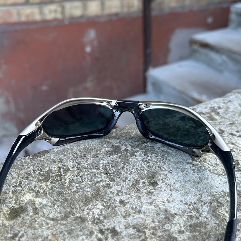 Puede incluir: Gafas de sol negras y plateadas con lentes oscuras. Las gafas tienen un dise&ntilde;o elegante y moderno con montura plateada y patillas negras. Las lentes son de un tono oscuro, proporcionando protecci&oacute;n solar.