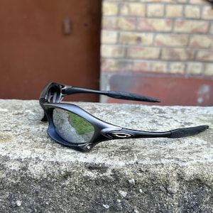May include: Black sport sunglasses with a curved frame and mirrored lenses. The sunglasses have a sleek, modern design with textured arms for a secure grip. The lenses reflect the surrounding environment, adding a dynamic visual element.