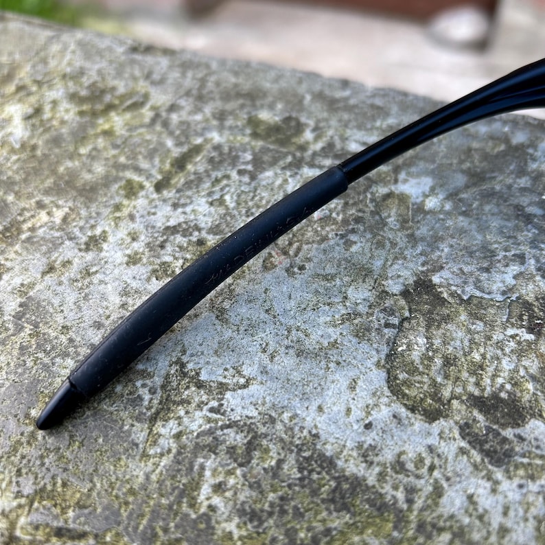Op de afbeelding: Close-up van een zwarte brilpoot met een rubberen grip. De tekst "MADE IN U.S.A." staat op de poot. De poot is gebogen en loopt taps toe naar een punt.