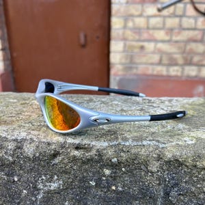 May include: Silver sunglasses with orange and yellow lenses. The sunglasses feature black earpieces and a modern design. The lenses reflect a vibrant array of colours, adding a stylish touch to the eyewear.