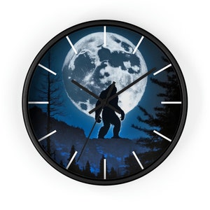 May include: A black wall clock with a silhouette of Bigfoot standing in front of a full moon. The background is a dark blue forest scene.