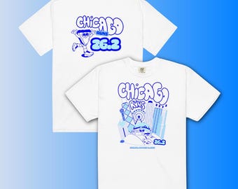 Könnte beinhalten: Zwei weiße T-Shirts mit blauen Grafiken. Ein Shirt zeigt eine Cartoonfigur und den Text "CHICAGO RUNS 26.2". Das andere Shirt zeigt eine Stadtlandschaft mit demselben Text. Beide Shirts sind kurzärmelig.