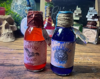 Puede incluir: Dos botellas de vidrio con etiquetas "Vampire Blood" y "Werewolf Blood". La botella roja contiene líquido rojo y un sello de cera. La botella azul contiene líquido azul y cuerda.