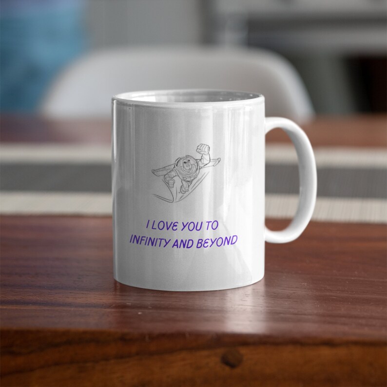 May include: White ceramic coffee mug with a black and white line drawing of Buzz Lightyear from Toy Story. The mug has the text "I love you to infinity and beyond" in purple.