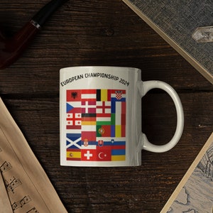 May include: White ceramic mug with a design of flags from different countries. The text "EUROPEAN CHAMPIONSHIP 2024" is printed on the mug.