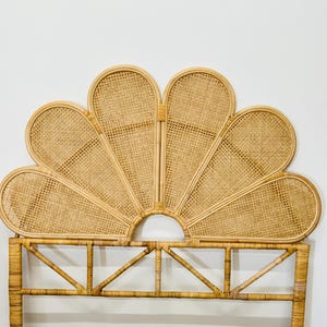 May include: A woven rattan headboard with a large, flower-shaped design. The headboard is made of natural, light brown rattan and has a simple, elegant design.