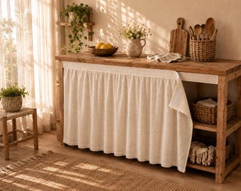 Könnte beinhalten: Eine Kücheninsel aus Holz mit einem beigen Stoffvorhang, der mit Klettverschlüssen befestigt ist. Die Insel verfügt über ein offenes Regal auf der rechten Seite mit zwei geflochtenen Körben, während auf der Oberfläche eine Schale mit Zitronen steht.