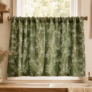 May include: A sage green cafe curtain featuring a delicate white embroidered floral vine pattern. The curtain is gathered on a wooden rod and hangs over a window, displaying a semi-sheer fabric with intricate stitched details throughout the design.