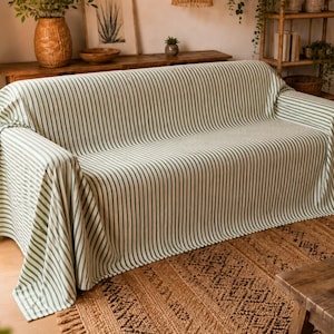 K&ouml;nnte beinhalten: Ein Sofa, das mit einer Stoffdecke mit vertikalen Streifen in Salbeigr&uuml;n und Cremewei&szlig; bedeckt ist. Das Textil liegt &uuml;ber der R&uuml;ckenlehne, der Sitzfl&auml;che und den Armlehnen des Sofas und bietet eine vollst&auml;ndige Abdeckung mit durchgehendem Streifenmuster.