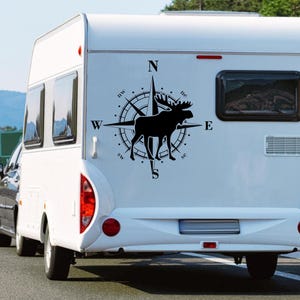 Könnte beinhalten: Schwarz-weißes Kompass-Dekor mit einer Elch-Silhouette auf einem weißen Wohnmobil. Der Kompass zeigt nach Norden, Süden, Osten und Westen. Der Kompass hat die Buchstaben N, S, E, W, NW, NE, SW und SE.