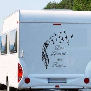 Op de afbeelding: Zwarte veer- en vogelzwermsticker op de achterkant van een witte camper. De sticker bevat de Duitse tekst "Das Leben ist eine Reise..." wat "Het leven is een reis..." betekent.