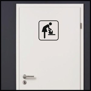 May include: A black and white sign with a symbol of a person changing a diaper. The sign is on a white door with a silver door handle.