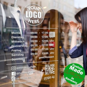 Op de afbeelding: Een wit bord met zwarte tekst op een glazen winkelruit. Het bord geeft de openingstijden voor elke dag van de week weer. Het bord bevat ook een QR-code, social media-pictogrammen en een telefoonnummer. Het bord luidt "YOUR LOGO HERE" bovenaan en "Custom Made in Germany" onderaan.