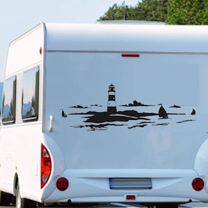 Op de afbeelding: Een witte camper met een zwarte silhouette-sticker van een vuurtoren, zeilboten en golven op de achterkant.