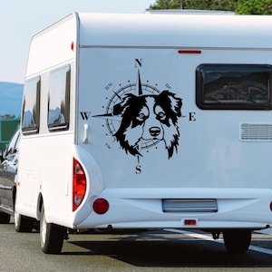 Könnte beinhalten: Eine schwarz-weiße Silhouette eines Hundekopfes mit einem Kompass-Design dahinter. Der Hund blickt nach vorne mit herausgestreckter Zunge. Der Kompass hat die Buchstaben N, S, E und W um den Rand herum. Das Bild befindet sich auf der Rückseite eines weißen Wohnmobils.