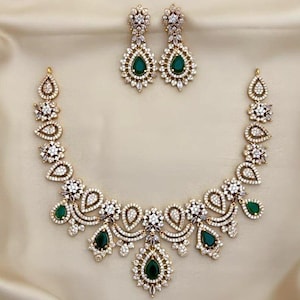 May include: A necklace and matching pair of drop earrings featuring a metallic setting encrusted with clear white crystals. The jewelry set incorporates multiple teardrop-shaped green stones arranged in a symmetrical floral pattern design.