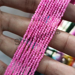 Könnte beinhalten: Nahaufnahme von mehreren Strängen kleiner, facettierter, leuchtend rosa Perlen. Die Perlen sind aufgefädelt und erzeugen einen zarten und schimmernden Effekt. Das Bild ist gut beleuchtet und hebt die Farbe und Textur der Perlen hervor. Die Perlen sind wahrscheinlich für die Schmuckherstellung.