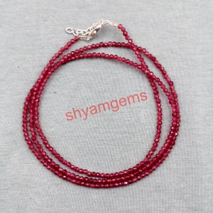 Könnte beinhalten: Eine mehrreihige Halskette aus kleinen, runden, tiefroten Perlen. Die Halskette hat einen silberfarbenen Verschluss und eine Kette. Der Text "shyamgems" ist in der Mitte des Bildes aufgedruckt.