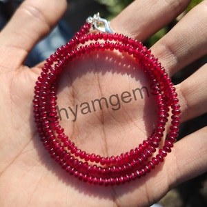 May include: A necklace composed of small, round, deep red beads. The beads are strung together, forming multiple strands. A silver clasp secures the necklace. The text "hyamgem" is visible in the image.