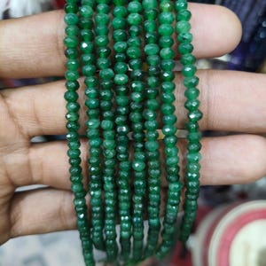 May include: Strands of faceted, emerald green gemstone beads. The beads are small, round, and strung together, creating a shimmering effect. The beads are a deep, rich green color, and the facets catch the light, adding sparkle. Ideal for jewelry making.