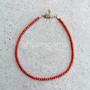 May include: A delicate red beaded bracelet with a silver clasp. The bracelet is made of small, round, red beads strung together. The clasp is a simple, secure design. The bracelet is shown on a gray surface.