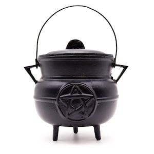 May include: A black cast iron cauldron with a lid and a handle. The cauldron has three short legs and a pentagram design on the front. The handle is made of black wire.