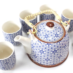 May include: A blue and white ceramic teapot with a brown rim and a bamboo handle. The teapot is surrounded by four matching teacups.