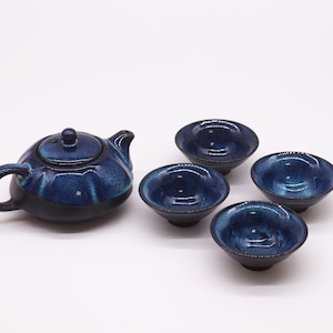 May include: A blue and black ceramic teapot and four matching teacups. The teapot has a rounded body and a lid with a small knob. The teacups are small and have a rounded shape.