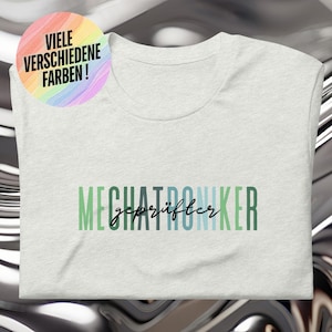 Puede incluir: Una camiseta gris claro con el texto "Mechatroniker" en un degradado arcoíris de verde, azul y blanco. El texto "geprüfter" está en negro debajo del texto arcoíris. El texto "VIele VERSCHIEDENE FARBEN!" está en un degradado arcoíris sobre un círculo blanco en la esquina superior izquierda de la imagen.