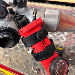 May include: A red and black fire hose nozzle with a built-in light. The nozzle is attached to a silver metal fitting and a red and tan hose. The text "SUR STRE" is visible on the nozzle.