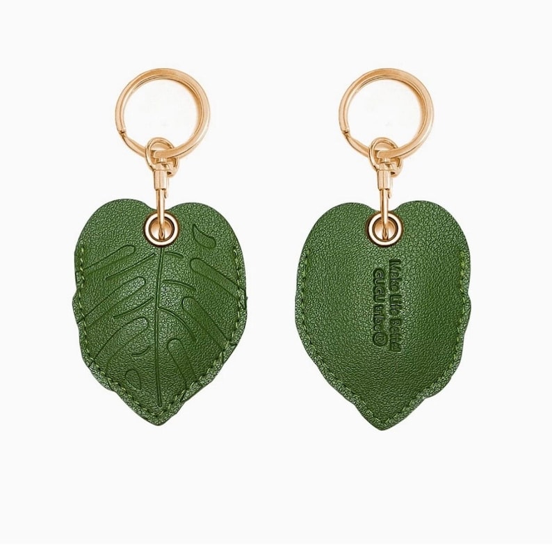 May include: A green leaf-shaped keychain with gold-colored hardware. The front of the leaf has a detailed vein pattern, while the back has the text "Made Life Better" in a circular design. The keychain is a decorative accessory.