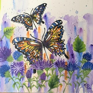 May include: A vibrant watercolor painting featuring two butterflies with orange, blue, and yellow wings, hovering above purple and blue flowers. The background has a watercolor wash of purple, blue, and orange.